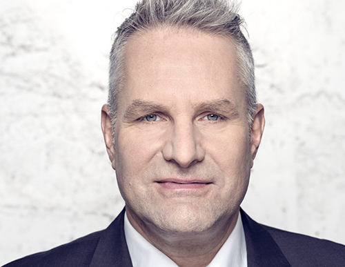 Portrait of Dr. Carsten Föhlisch in a dark suit in front of a light wall.